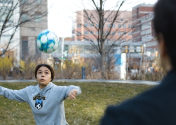 A female soccer player looks up as she heads a soccer ball. 