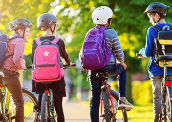 Children ride their bikes down a sidewalk with their backs facing the camera. 
