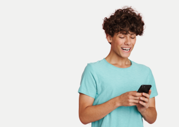 A young teen in a green shirt looks down at his cell phone and smiles. 