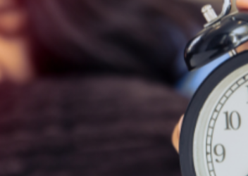 A teenager lays down and reaches for an alarm clock after having trouble sleeping.