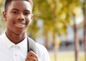 A teenager wearing a white shirt smiles while wearing a backpack. 